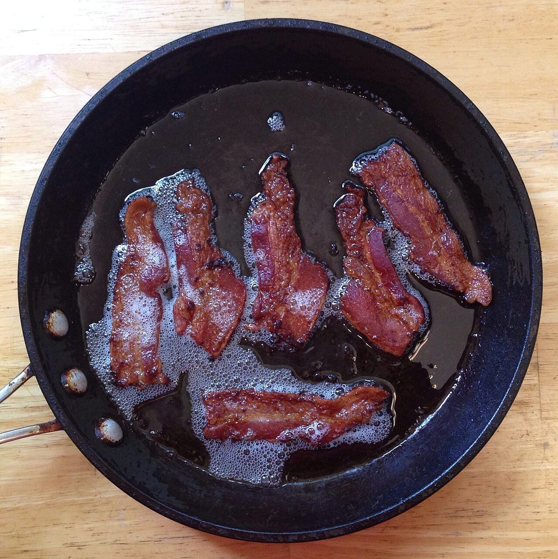 Bacon frying in a pan with rendered fat pooled around it