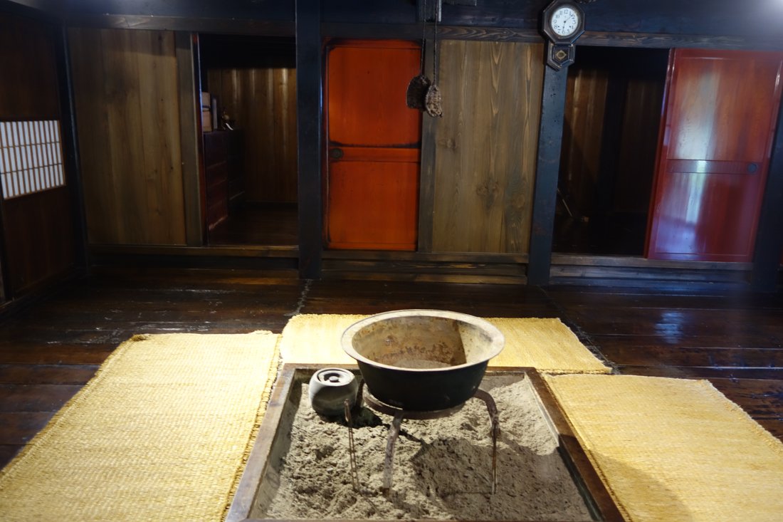An irori — the sunken square hearth, its ash bed, and a pot set over it. This is the photograph I went looking for