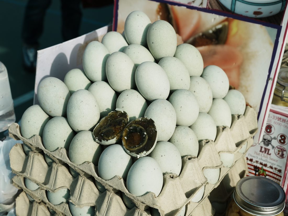 Century eggs in their preserving coating, one cracked open to show the dark interior