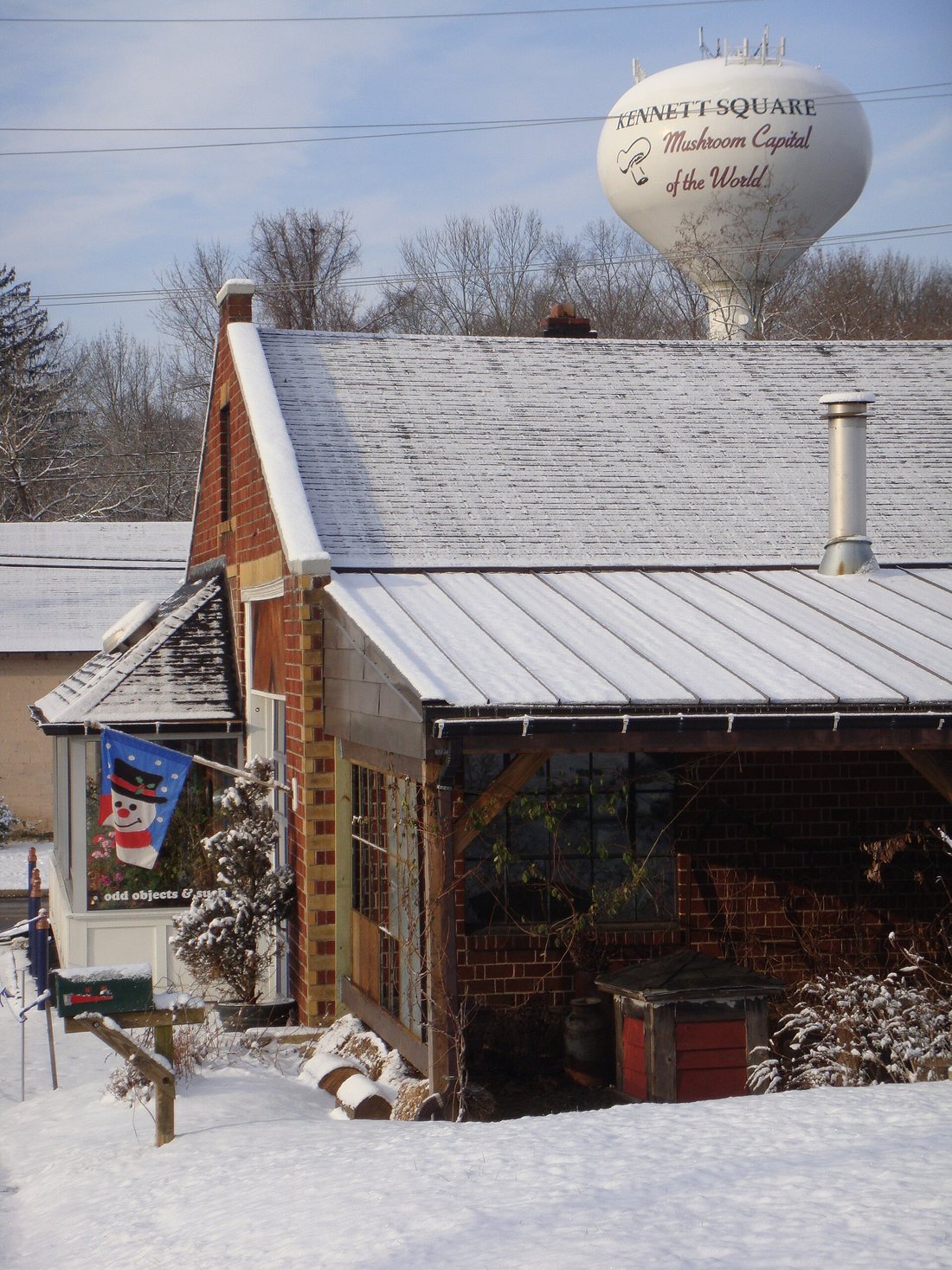 A snowy street in Kennett Square with a water tower behind lettered "Kennett Square, Mushroom Capital of the World"