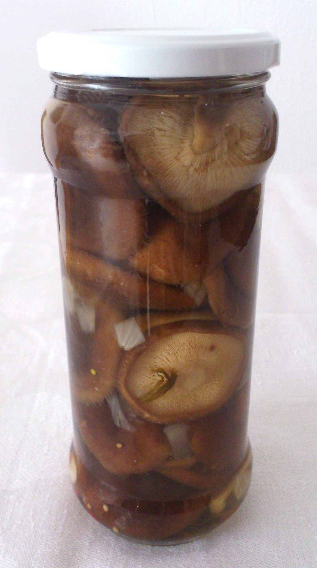 A tall glass jar packed with marinated brown mushrooms and onion