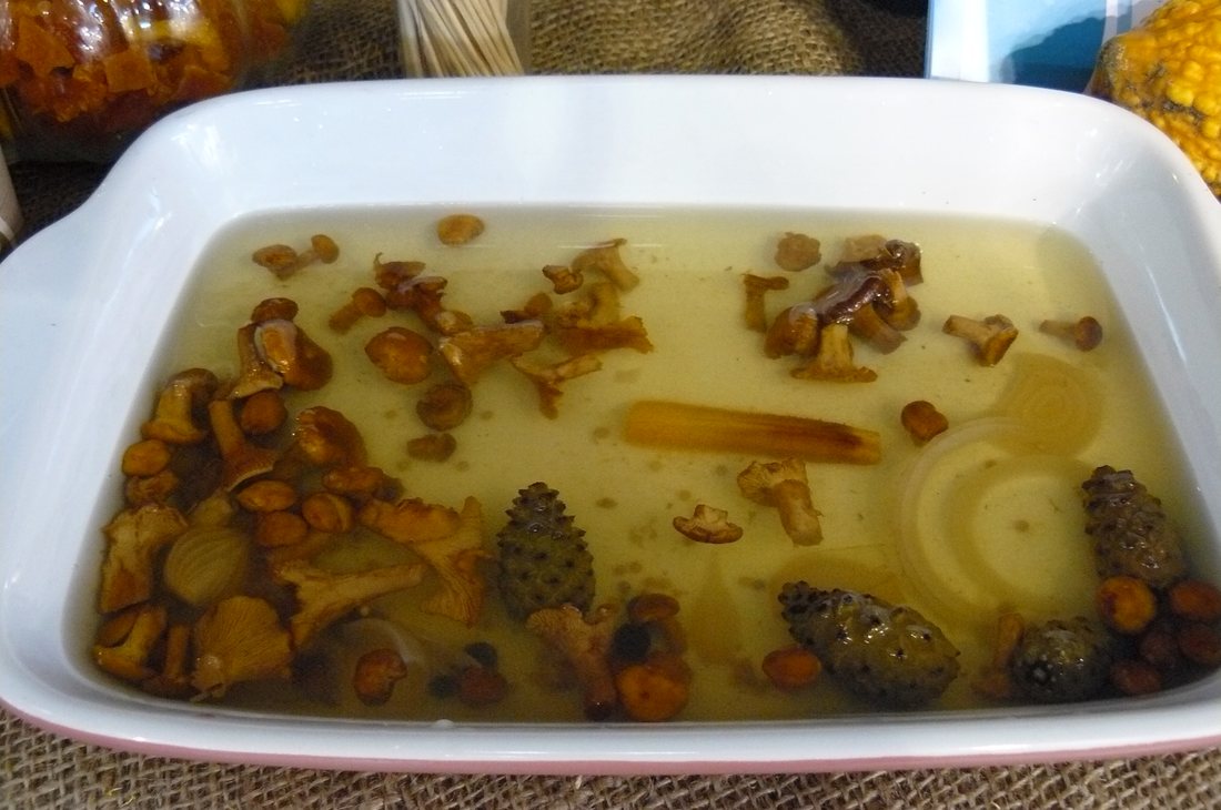 A baking dish of mushrooms in brine with onion and a pine cone, at a regional food fair in Poznań