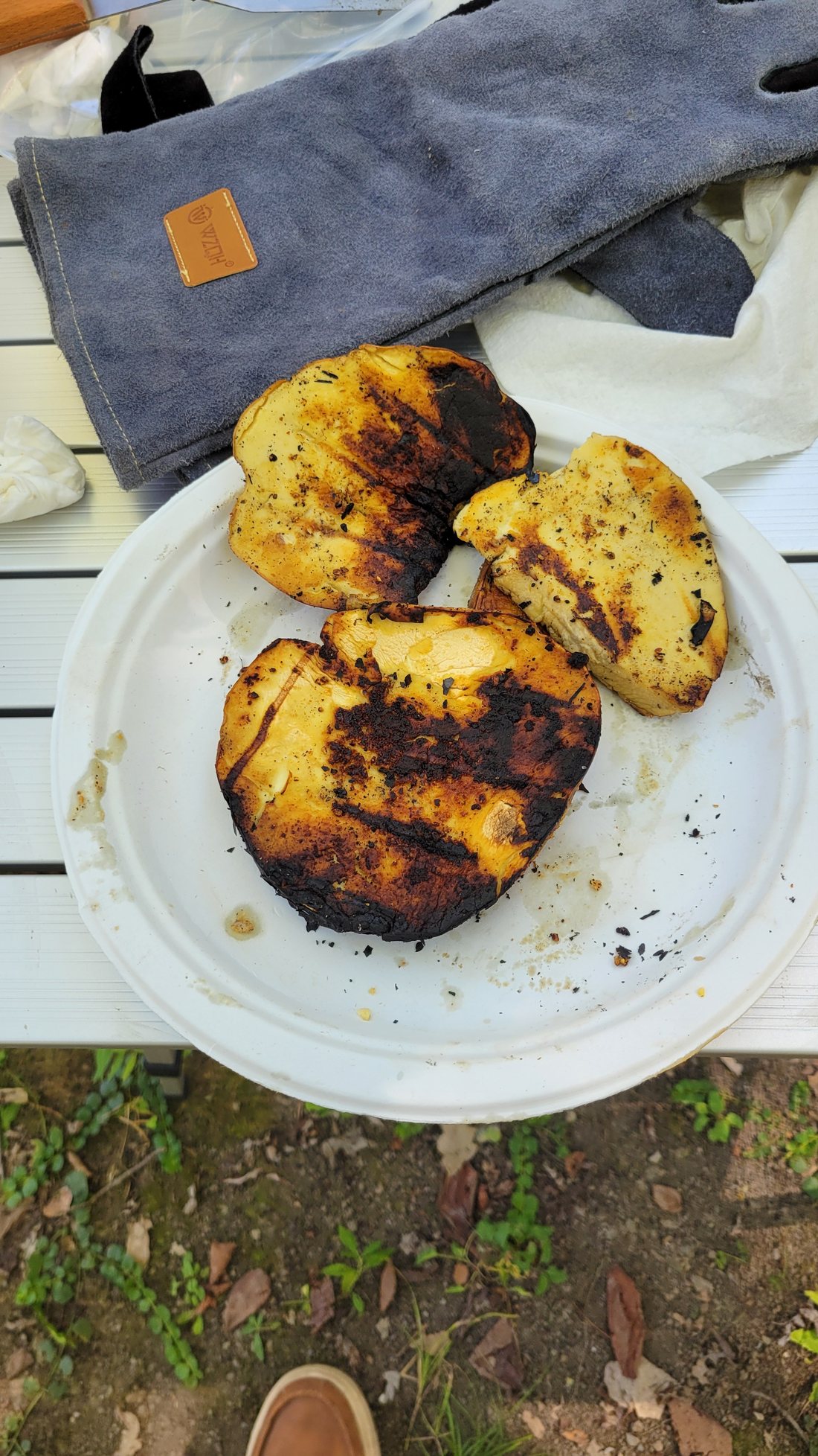 Three grilled giant puffball slabs on a paper plate, golden with butter and striped with black char from the grate