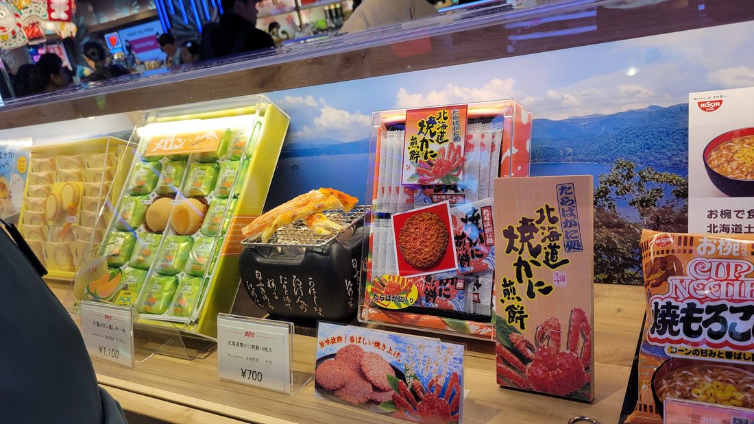 The Hokkaido counter — 北海道限定 grilled-crab senbei and 焼きもろこし among the boxes