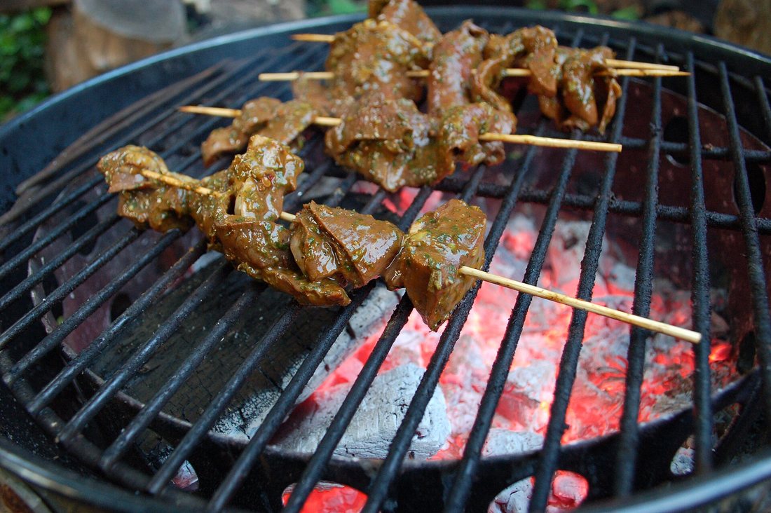 Marinated beef-heart anticuchos on bamboo skewers over a charcoal grill