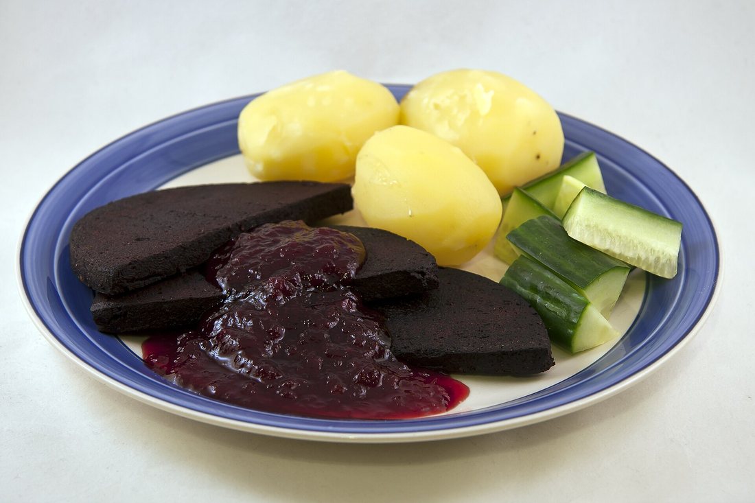 Slices of Swedish blodpudding with lingonberry jam, boiled potatoes and cucumber