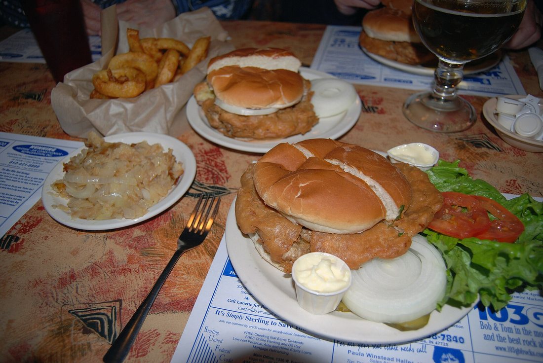 Fried brain sandwiches on buns with onion and pickles on a diner table, with fries behind