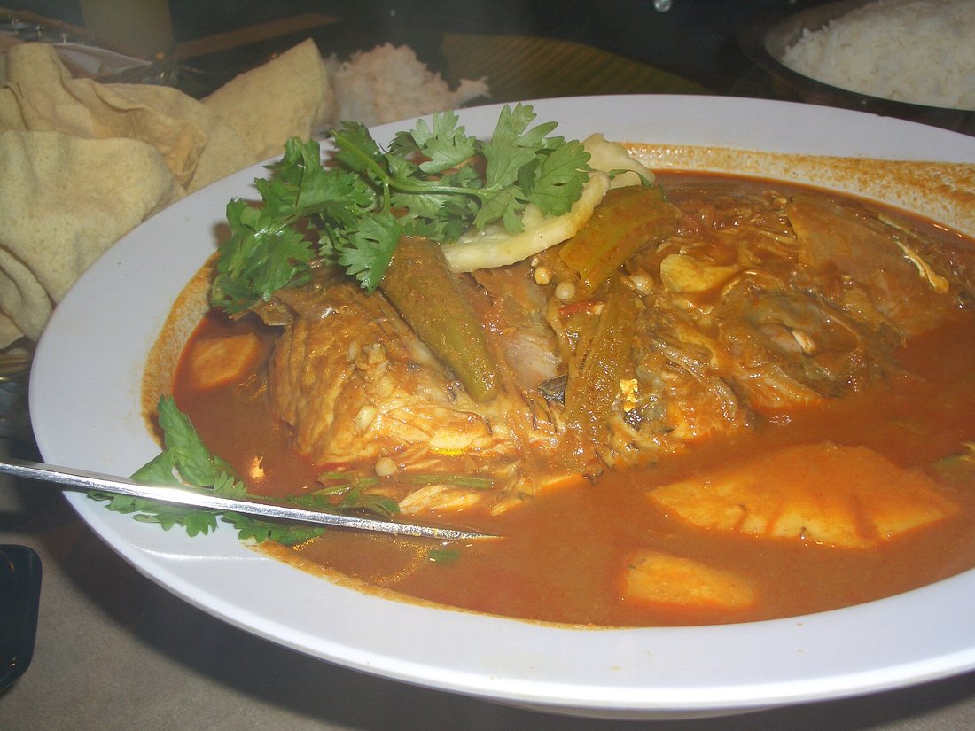 Fish head curry in a wide bowl with okra and coriander, with papadums and rice behind