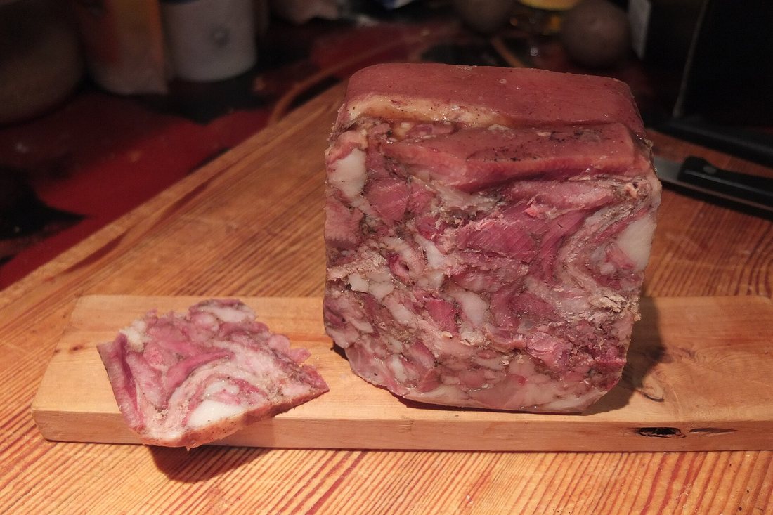 A block of Norwegian head cheese (hodesylte) on a board, with one slice cut to show meat set in aspic