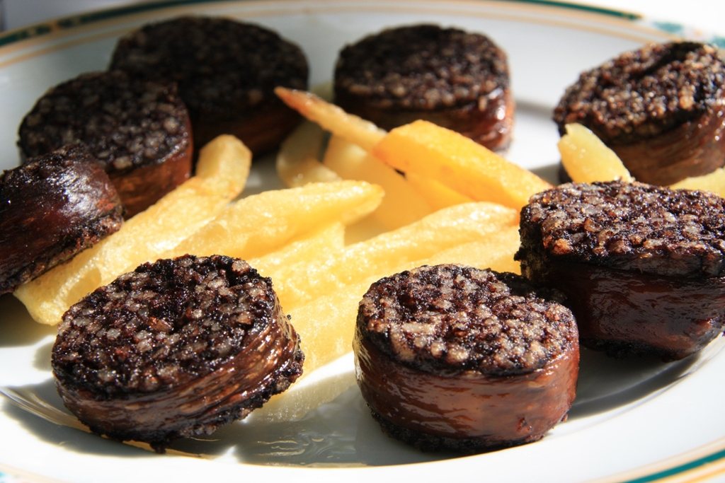 Pan-fried rounds of morcilla de Burgos, with grains of rice visible, next to fries