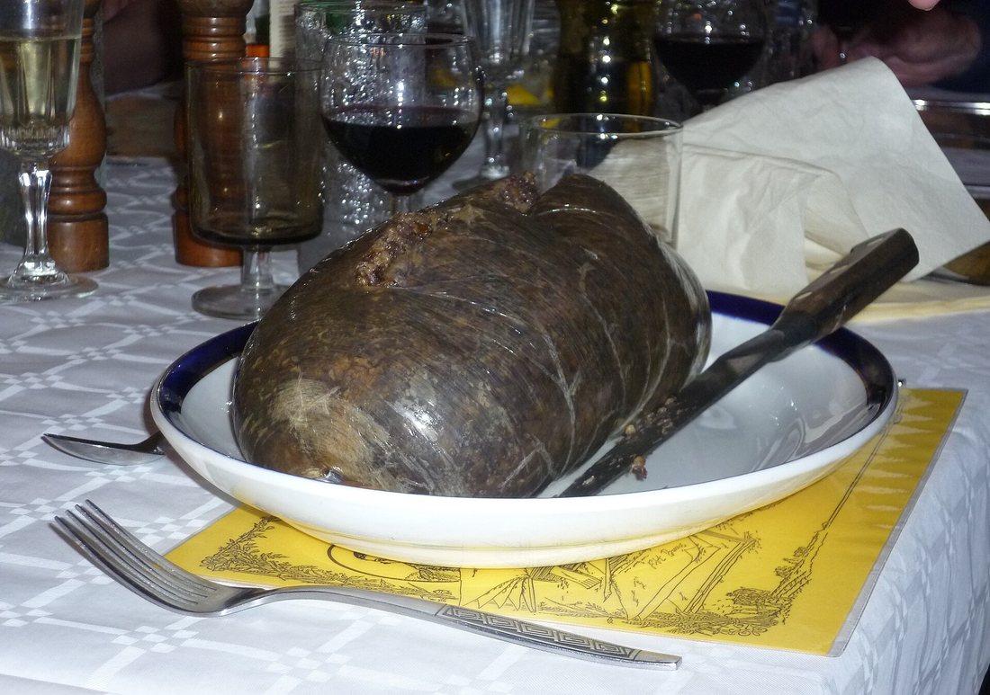 A whole haggis in a bowl with a knife beside it on a set dinner table