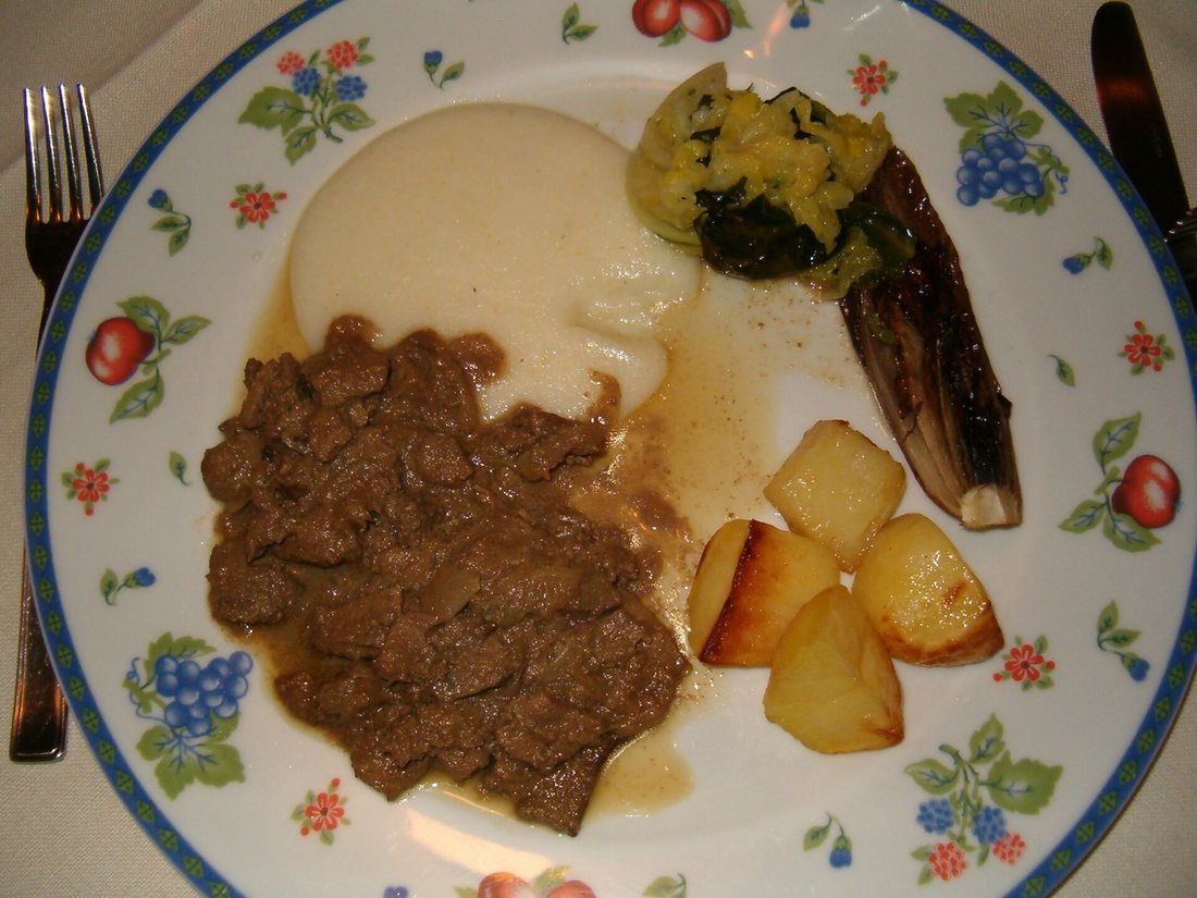 Fegato alla veneziana on a plate with white polenta, roast potatoes and grilled radicchio