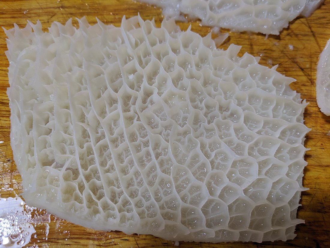 A sheet of raw white honeycomb tripe on a wooden board