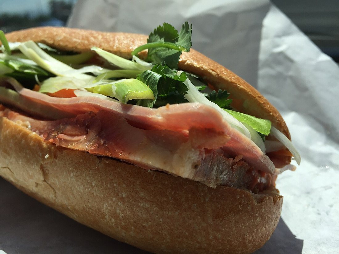 A bánh mì thịt nguội cut open, filled with sliced cold cuts, cucumber, pickled vegetables and herbs