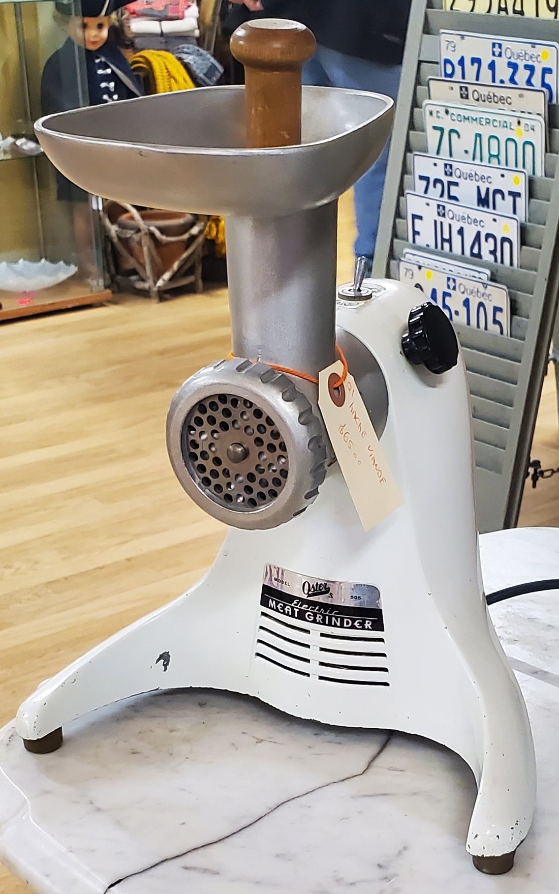 A white electric meat grinder with a steel hopper and grinding plate on a marble counter