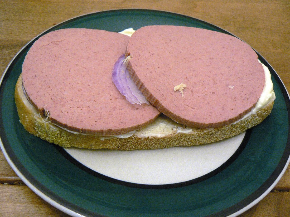 Two round slices of pink liverwurst on buttered bread with a sliver of red onion