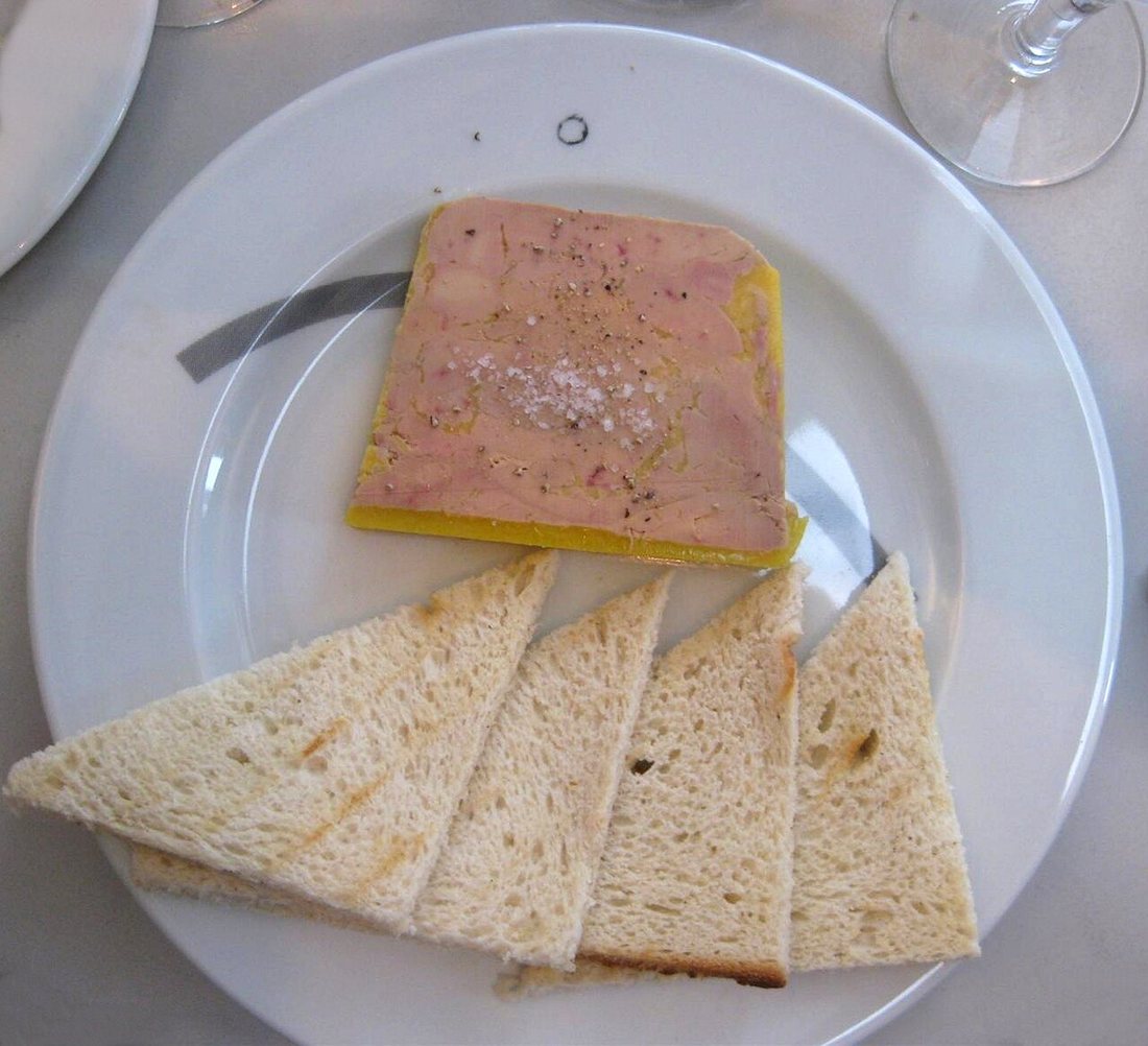 A rectangular slice of foie gras terrine with a thin yellow rim of fat and coarse salt, beside triangles of toast