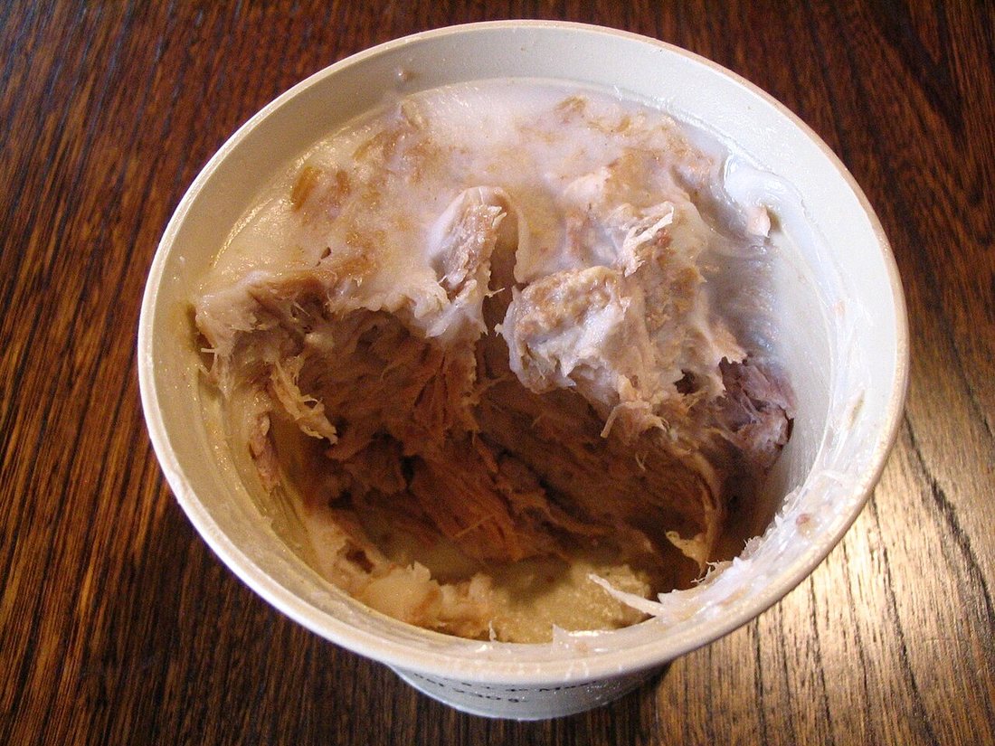 A white bowl of shredded brown rillettes under a cap of white fat, partly scraped back