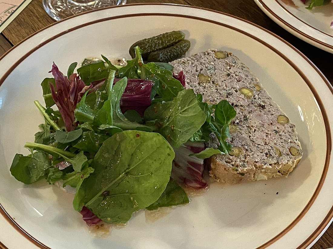 A slice of coarse pâté de campagne flecked with green peppercorns beside a salad of mixed leaves and two cornichons