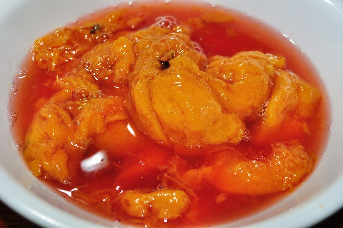 Pickled peaches — orange fruit in a spiced, faintly red syrup. Whole spices, not ground, and the fruit still holding its shape