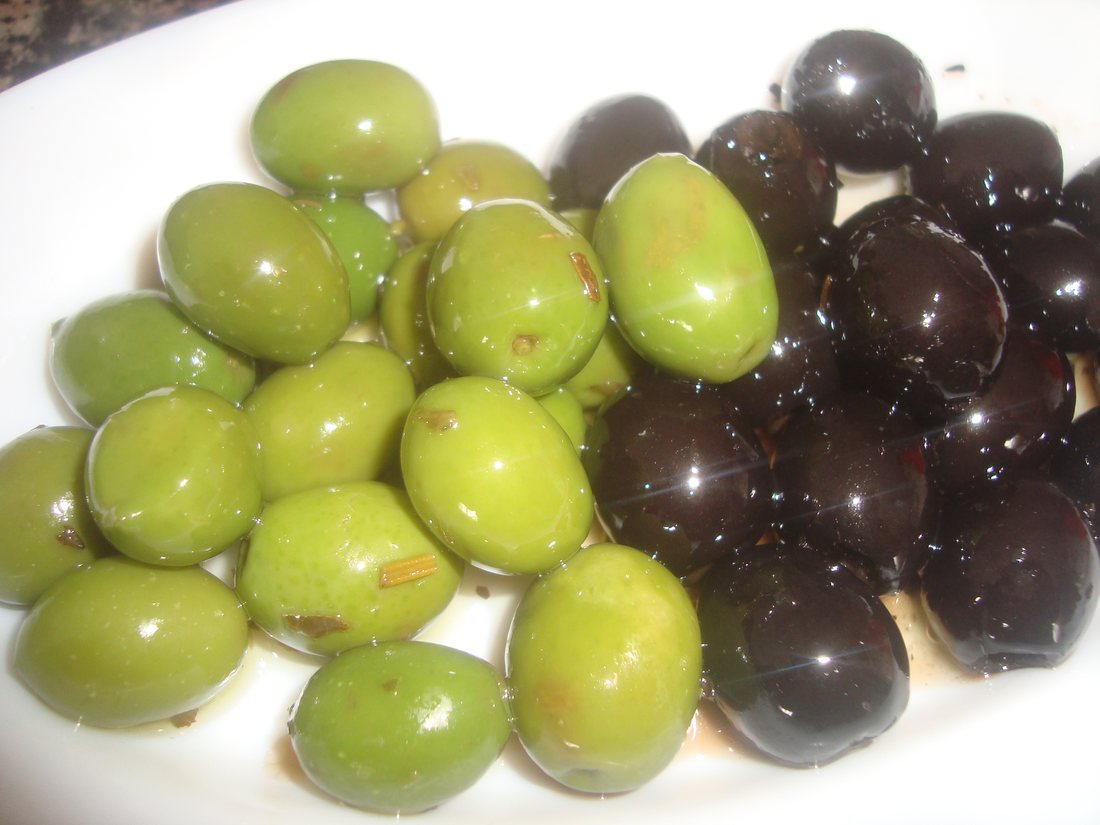 Big pale-green olives and glossy purple-black ones tipped together into a white dish. They look like two different fruits and they are one species — what separates them is when they were picked and what was done to them afterwards