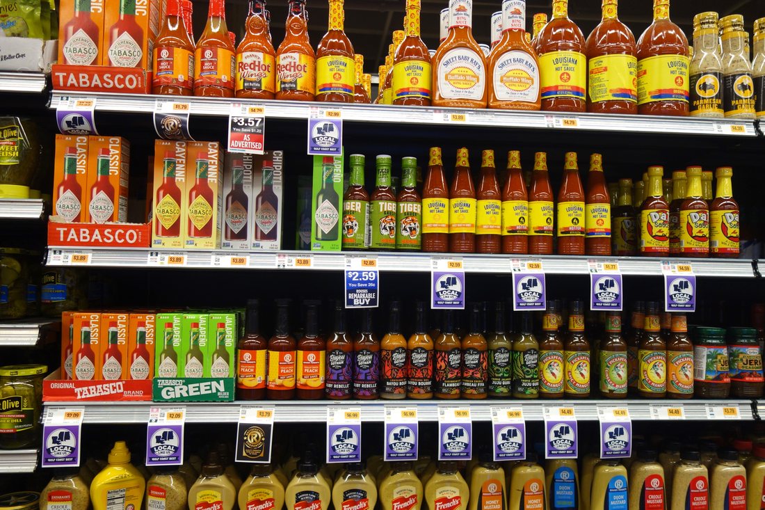 A supermarket hot-sauce shelf in New Orleans, four rows deep — Tabasco in several varieties on the left, Louisiana and Frank's RedHot across the middle, mustards below