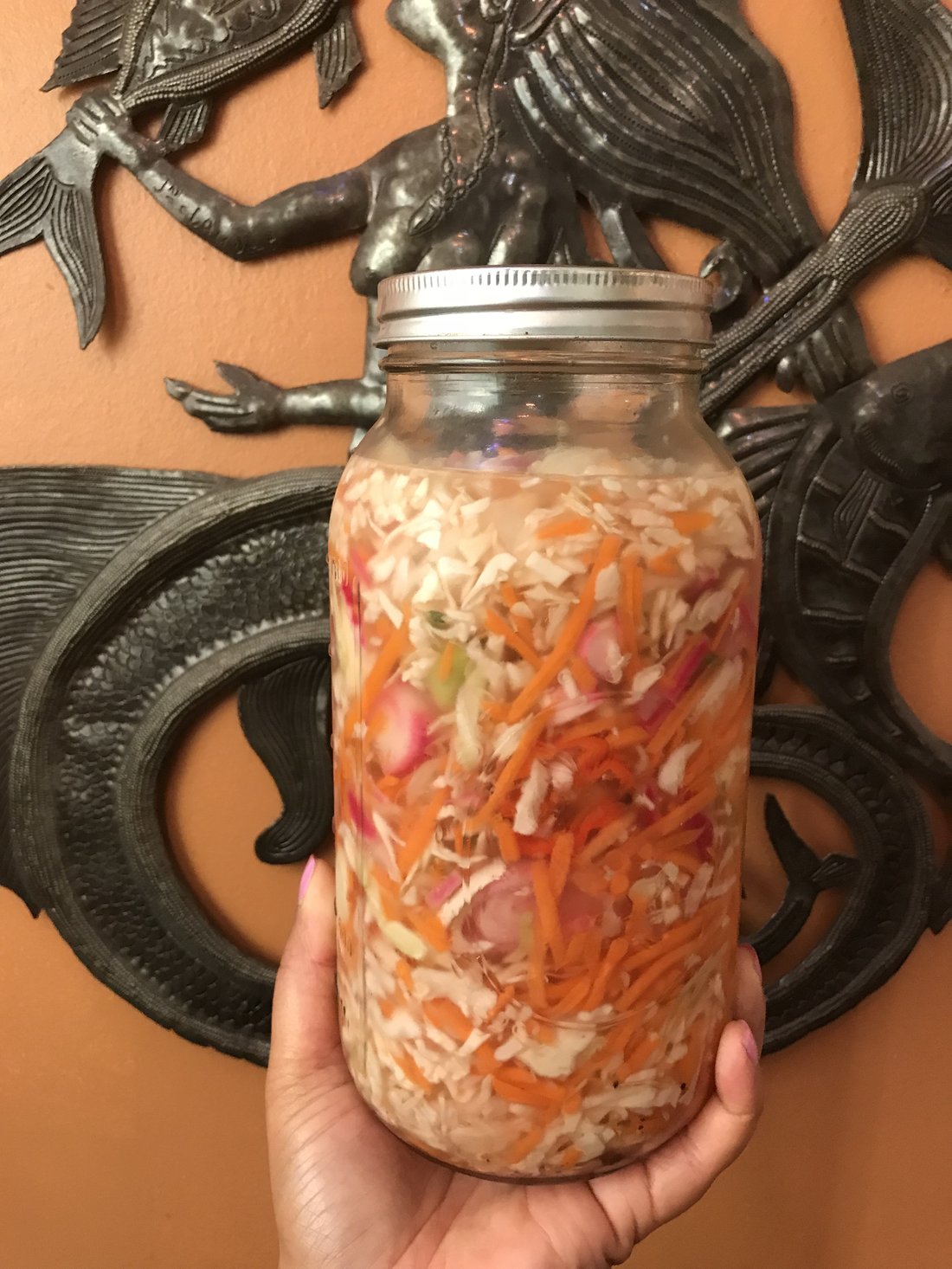 A jar of Haitian pikliz — shredded cabbage and carrot with scotch bonnet. Packed tight, because it settles