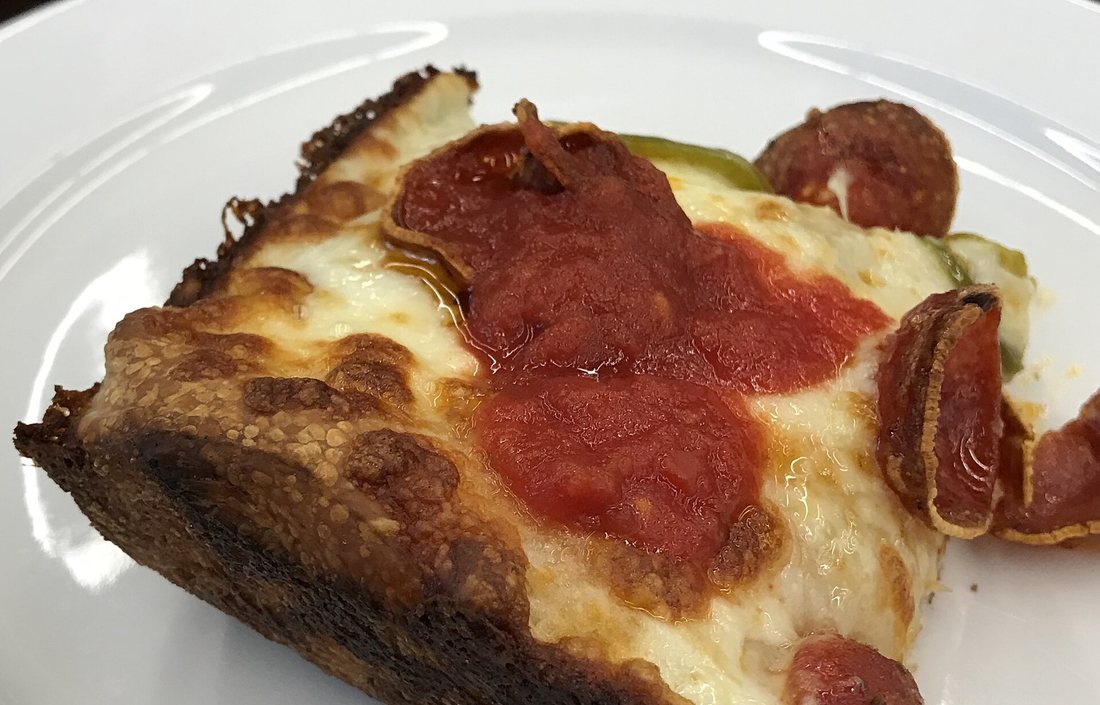 A square slice of Detroit-style pizza with pepperoni, sauce on top, and a dark lacy crust of fried cheese at the edge