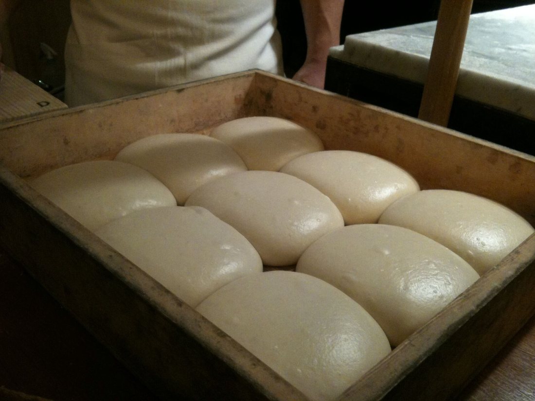 Pizza dough balls proofed and touching one another in a wooden dough box in a pizzeria