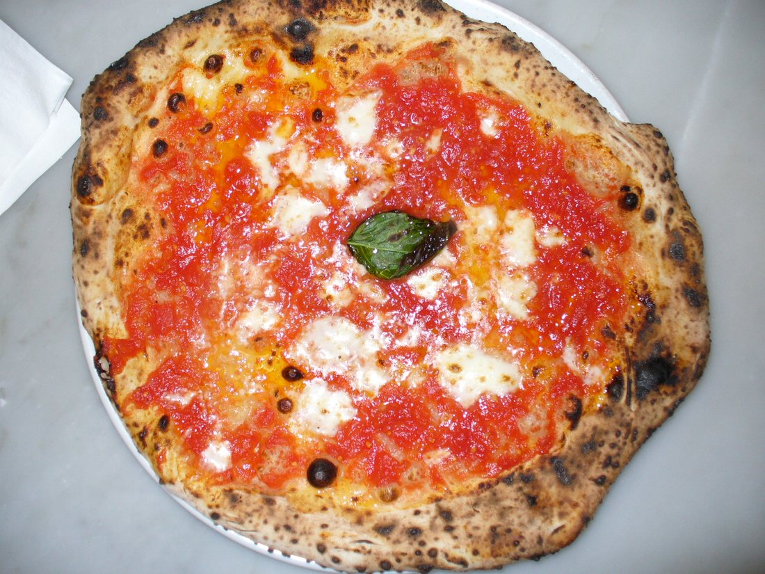 Top view of a Neapolitan Margherita with tomato, patches of mozzarella, a single basil leaf and a leopard-spotted rim