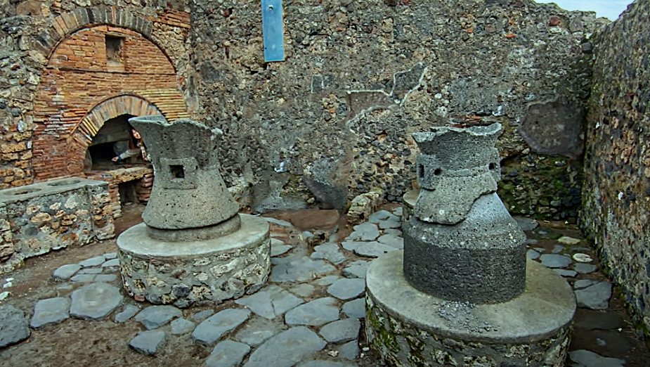 Ruins of a Pompeii bakery: two hourglass-shaped lava millstones in front of a brick-arched bread oven