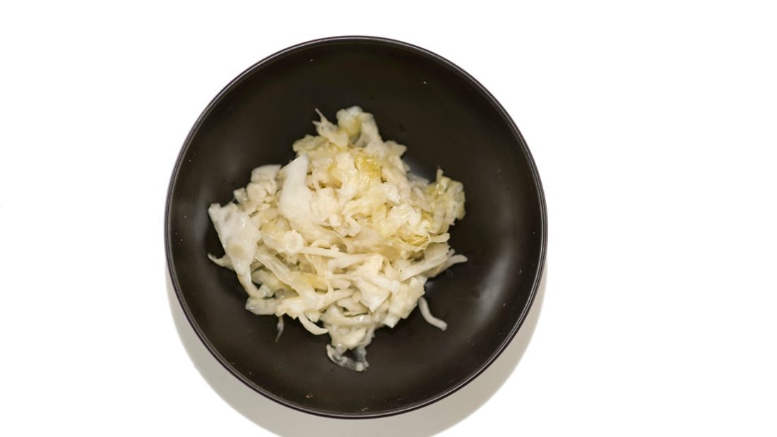 A ceramic fermentation crock and glass jars of bubbling sauerkraut and kimchi on a kitchen counter