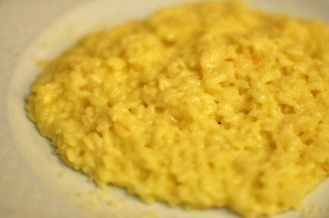 A shallow bowl of creamy saffron-yellow risotto, a wooden spoon resting in it