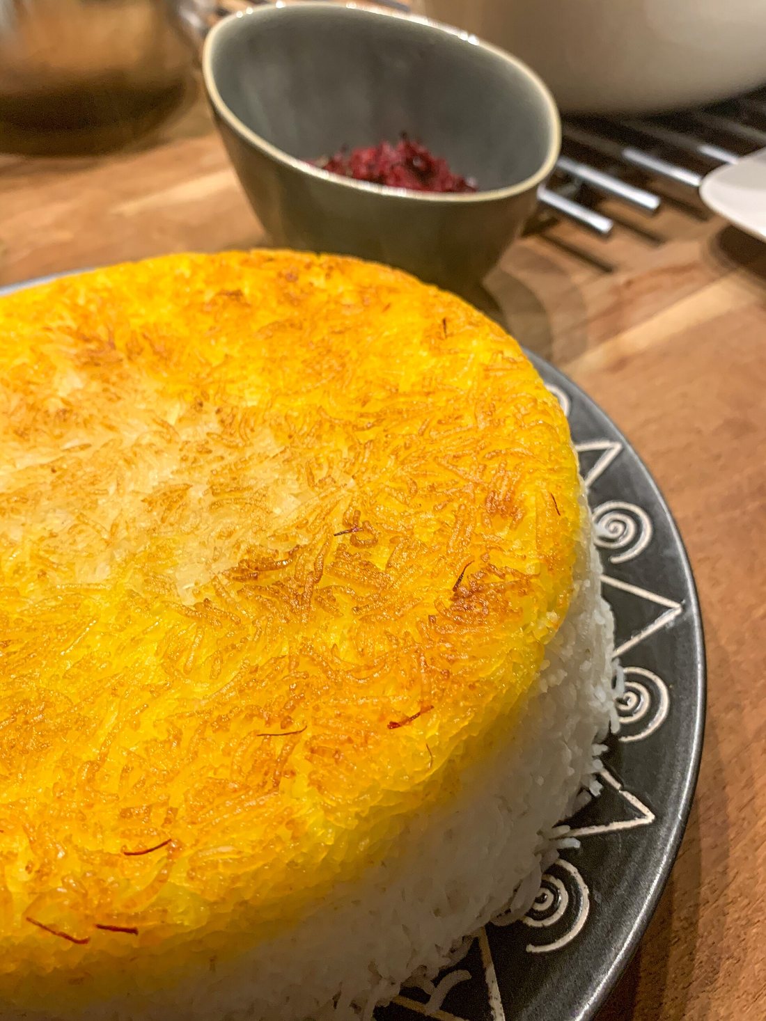 A mound of white long-grain rice turned out of the pot, capped with a golden saffron tahdig crust, a bowl of barberries behind