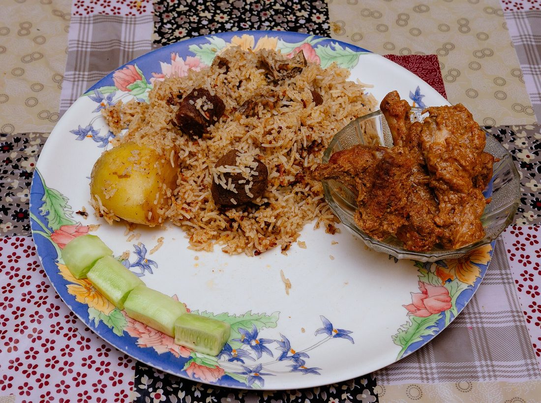 A pot of dum biryani opened at the table — distinct layers of long saffron-streaked rice over dark spiced meat, steam rising, fried onions and mint scattered on top