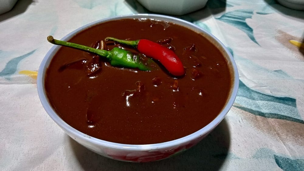 A bowl of dinuguan, the sauce nearly black and glossy, with vinegar sharpening it — blood as the thickener of a stew rather than the body of a loaf