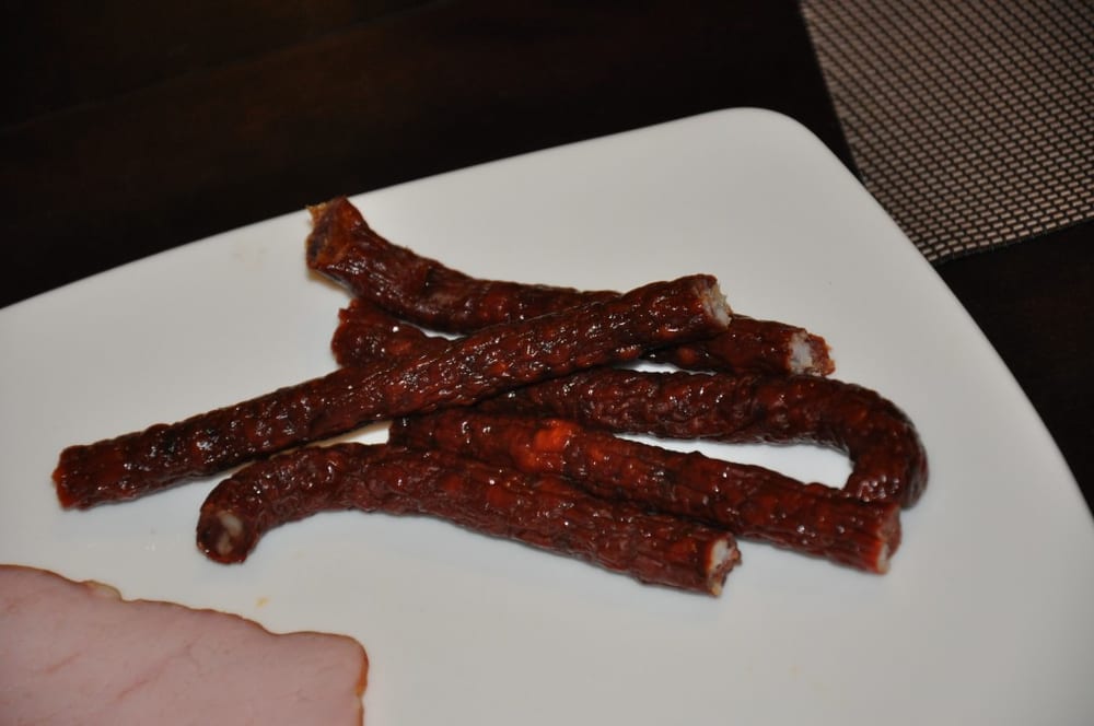 Snack sticks hanging on a smokehouse stick, pencil-thin and already deep mahogany. At 19-21 mm there is almost no interior left — the dried, smoked outer layer is most of what you're eating, which is why these overtake smoke faster than anything else on the rack