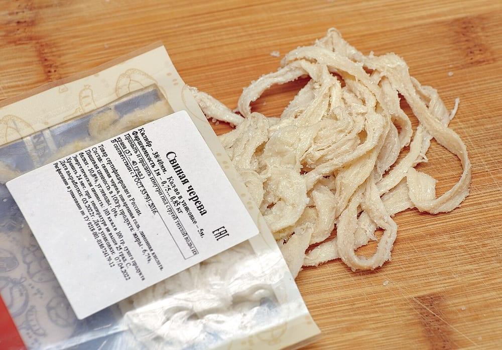 Salted natural hog casing beside a packaged manufactured casing — the natural one irregular and translucent, the manufactured one made to a number