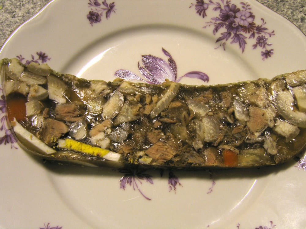 A cut head cheese terrine, irregular chunks of dark and pale meat suspended in clear amber jelly — nothing ground, nothing emulsified, the set entirely gelatin cooked out of the animal's own connective tissue