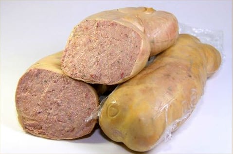 A coarse country pâté cut open in its terrine beside a length of liver sausage — identical batter, identical technique, two completely different social positions