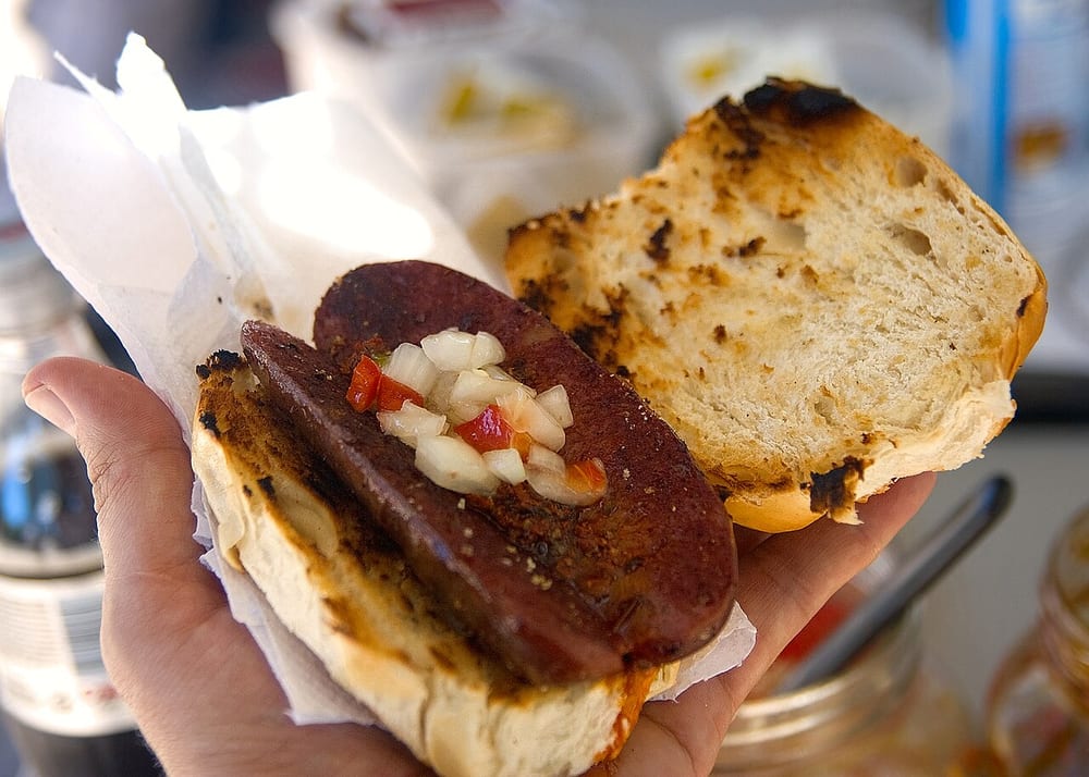 An Argentine chorizo butterflied and grilled, tucked into a crusty roll with chimichurri — the choripán