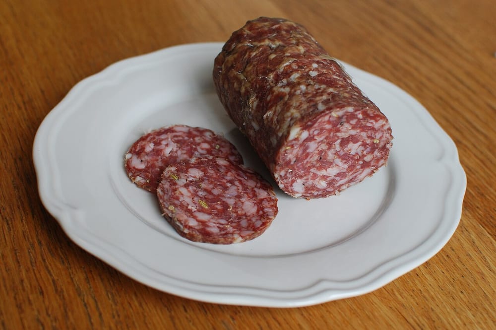 A wide finocchiona salami half-sliced, the coins soft and dark red, whole fennel seeds scattered through the fat