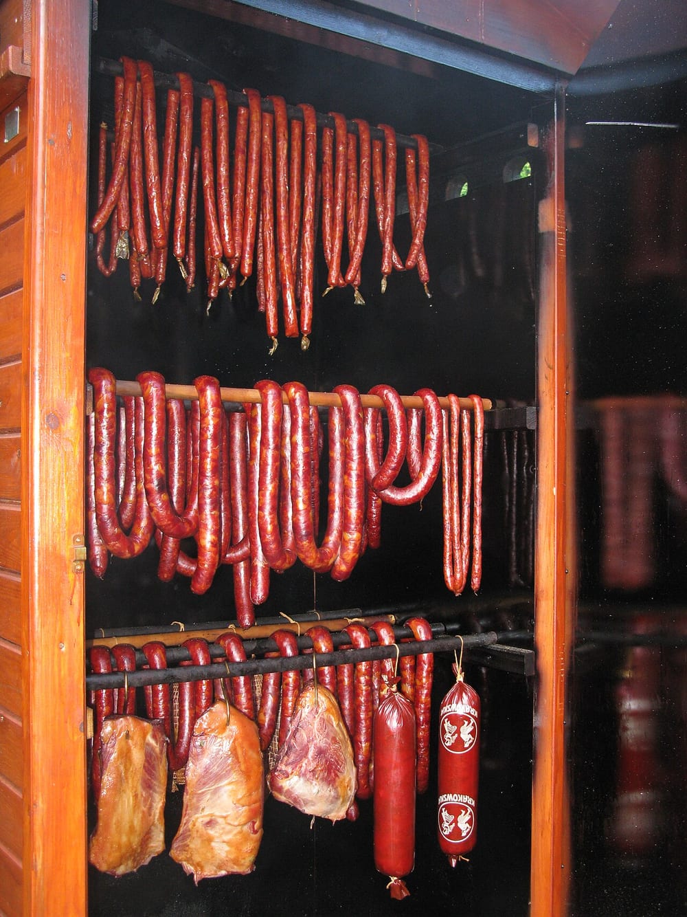 A rack of smoked kielbasa coils hanging in a smokehouse, the casings gone deep mahogany after blooming