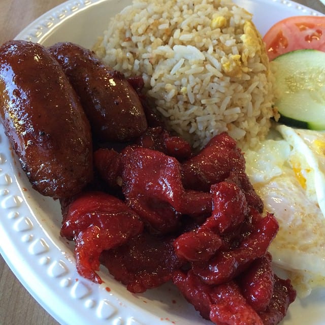 Fat stubby longganisa frying in their own rendered fat, glazed and darkly caramelized, beside garlic rice and a fried egg