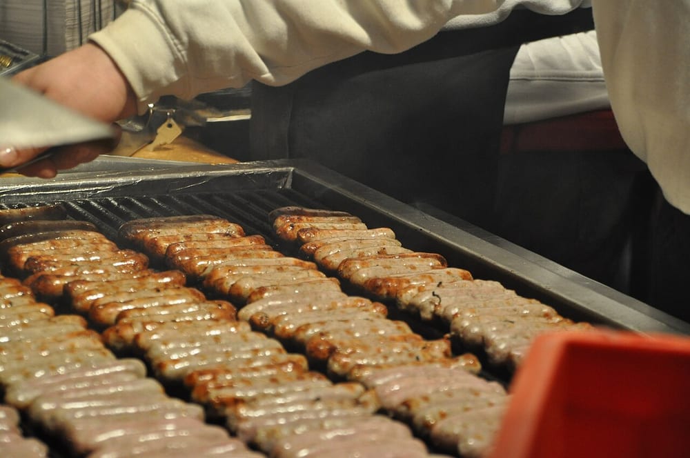 Six tiny Nürnberger bratwurst on a beechwood grill, each barely the length of a finger, browned and blistered in sheep casing