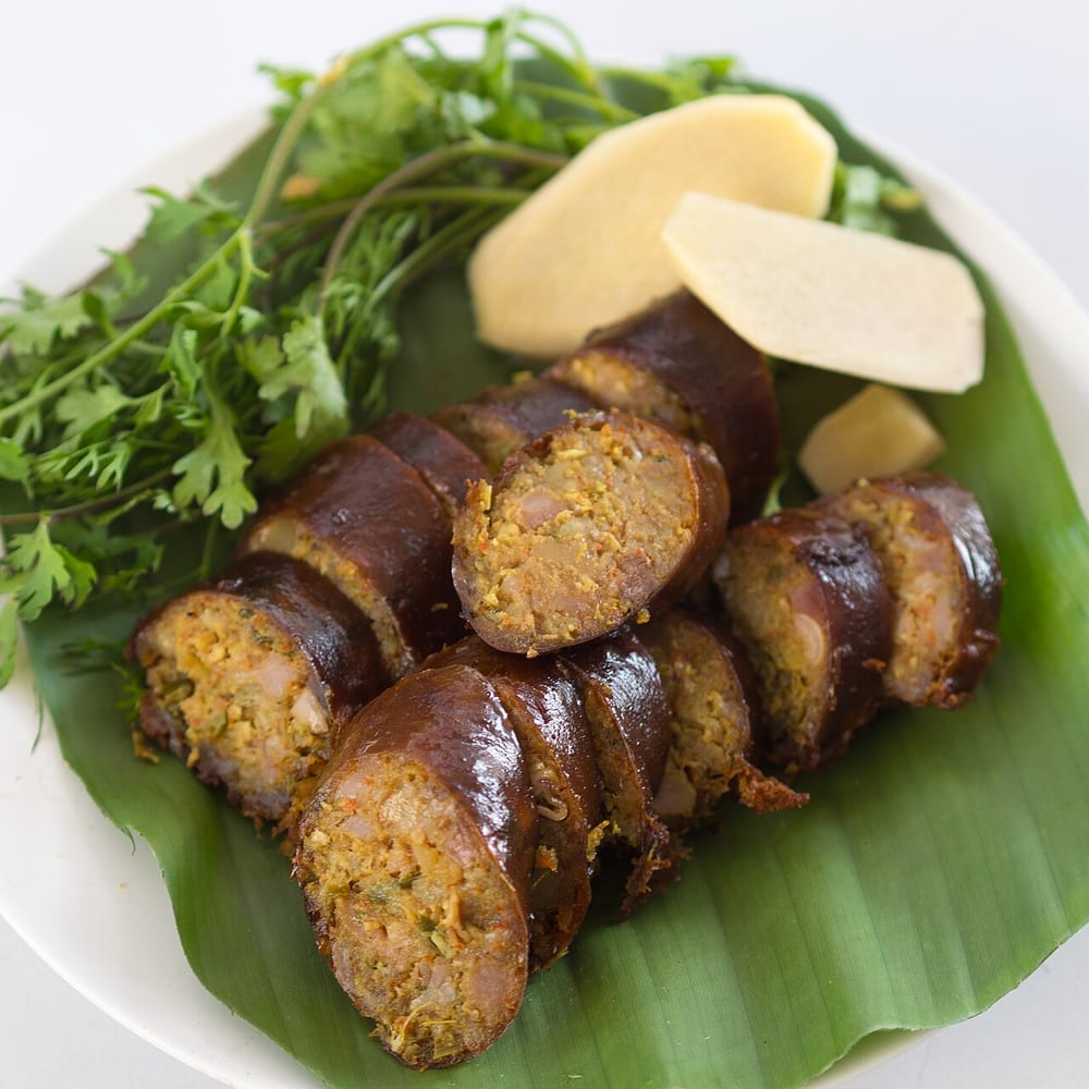A coil of sai ua on a banana leaf, deep yellow-orange from turmeric and flecked with lemongrass and lime leaf, one end sliced across