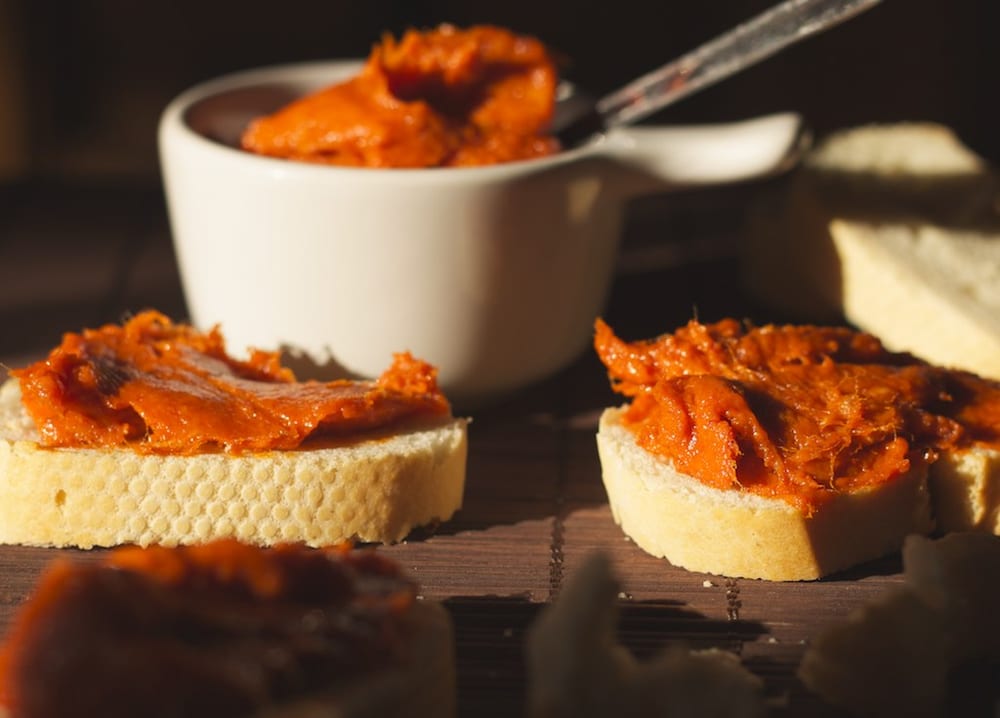 A cut sobrasada with a knife lifting a soft brick-red paste out of the casing and spreading it onto bread — this one never firms up