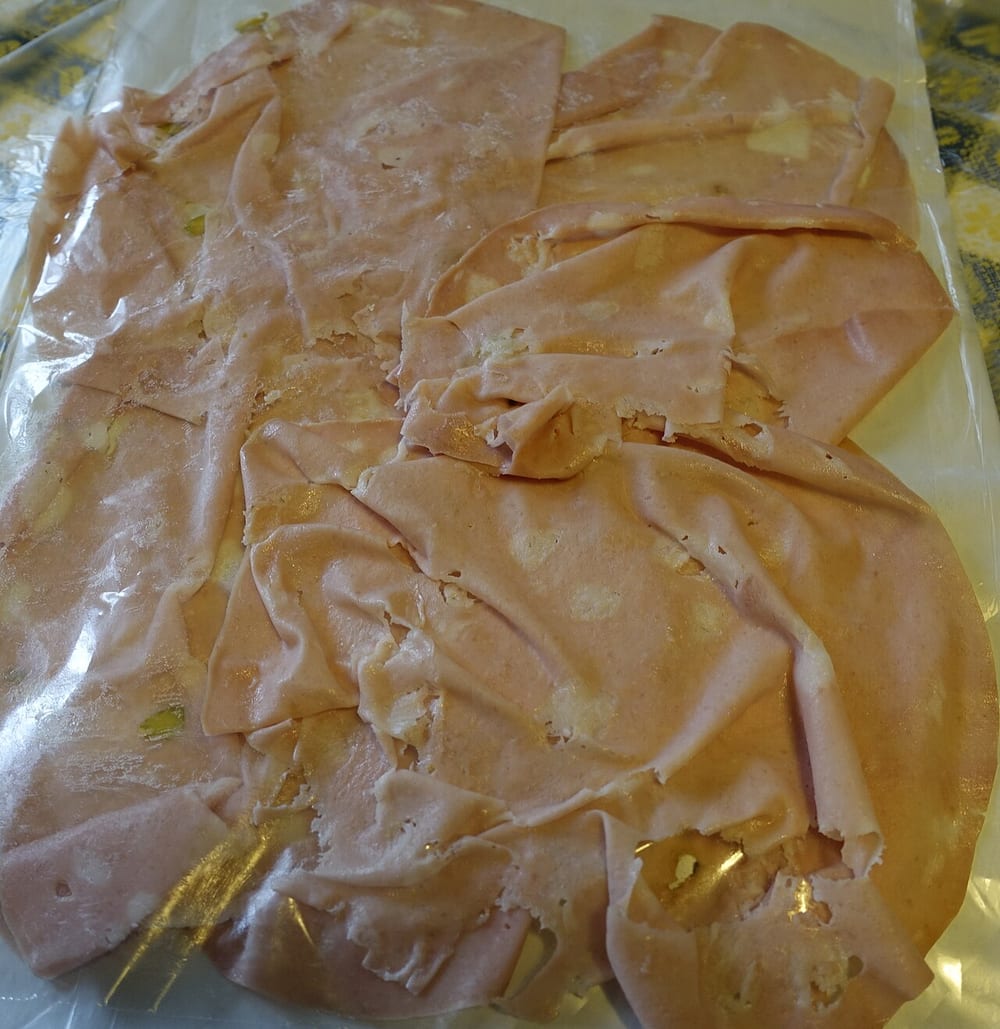 A slice of mortadella, the cut face perfectly smooth pink with white fat cubes suspended in it like inclusions in amber. The pink is emulsion; the cubes were placed there by hand — this is not a coarse grind