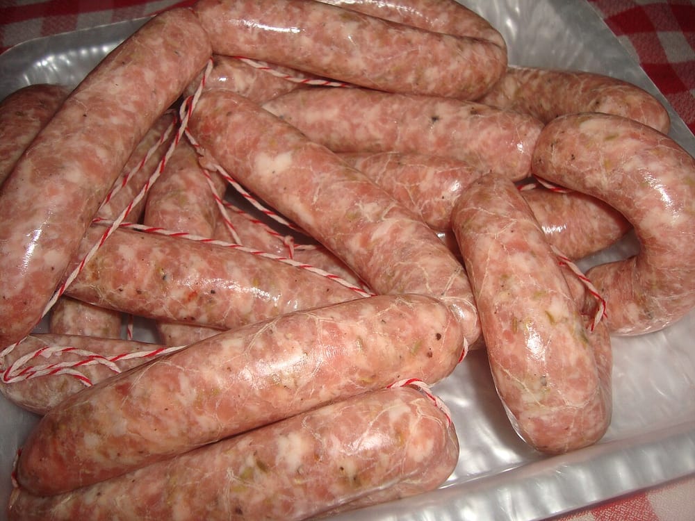 A coil of fresh coarse-ground sausage in natural hog casing, raw and pale pink, the fat still in visible white flecks rather than smeared — that flecking is the whole tell for a fresh sausage ground at the right temperature