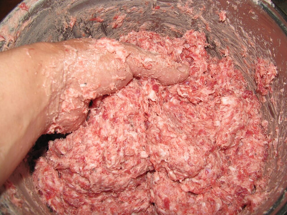 Coarse-ground pork and back fat in a chilled steel bowl, still showing individual strands and distinct white flecks of fat